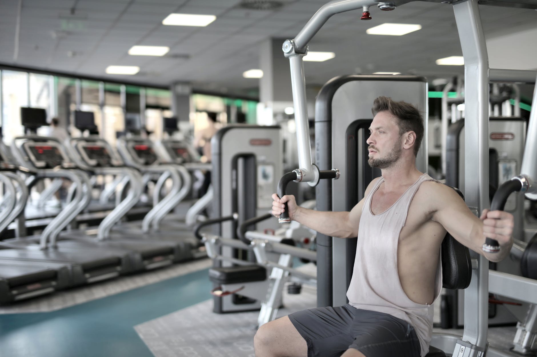 man in white tank top and grey shorts sitting on exercise equipment